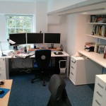 My desk, PC with three monitors. Shelves in an alcove on the right.